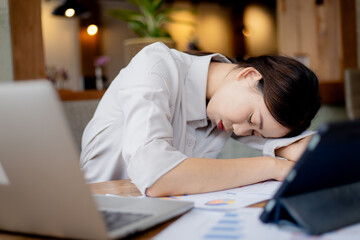 Overworked young businesswoman sleeping at office desk with laptop, symbolizing exhaustion, stress, deadlines, workplace challenges, and modern professional lifestyle.
