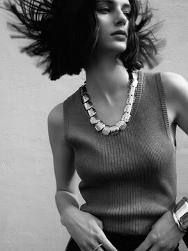 Woman with bob hairstyle wearing a grey sleeveless top and necklace in a dynamic pose.