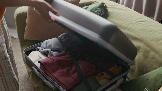Unrecognizable young woman finishing packing and closing her suitcase, ready for travel, vacation, or business trip