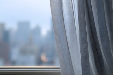 Sheer curtain framing window with soft city background.