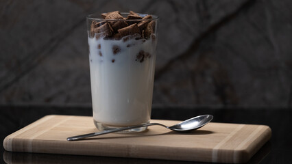 Glass of milk with chocolate cereal on wooden board