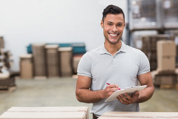 Male warehouse worker checking inventory with clipboard and pen in large warehouse, copy space