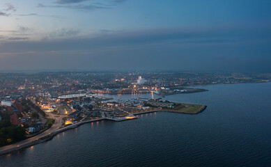 Fototapeta premium Aerial night view of Thisted, Denmark. Town lights, marina, Limfjord coastline, and surrounding neighborhoods create a tranquil Nordic cityscape under a twilight sky