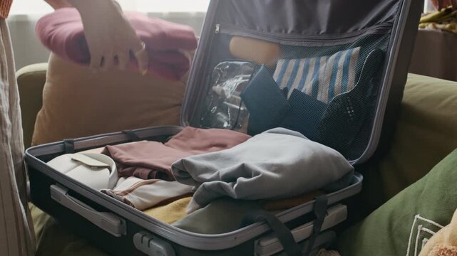 Cropped shot of unrecognizable woman carefully packing suitcase with neatly folded clothes, preparing for vacation, organized and ready for travel