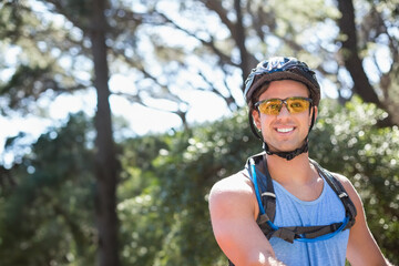 Man pausing on sunlit park trail wearing bicycle helmet, glasses and hydration pack, copy space