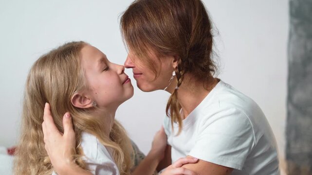 Tender moment of mother and daughter touching noses, showing affection and family love. Warm hug and close emotional connection in cozy home atmosphere