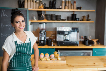 Female barista wearing striped apron handling pastry board and espresso machine at cafe, copy space