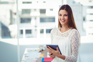 Fototapeta premium Woman in lace blouse smiling by window holding tablet at office desk with papers, copy space