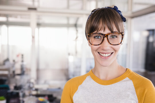 Woman standing at open plan office wearing fabric headband and tortoiseshell eyeglasses, copy space