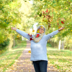 happy cheerful woman in autumn park throwing up colorful leaves