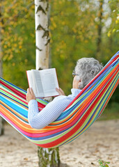 Relaxed Senior woman Reading in a Hammock by the Lake in Autumn