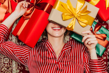 Smiling person in red striped pajamas lying with gifts on Christmas Eve