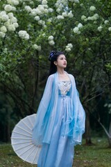 A young woman in a beautiful blue hanfu holding a parasol in a serene outdoor setting.