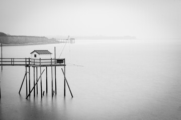 Cabane de pêche sur pilotis se reflétant dans une mer calme

