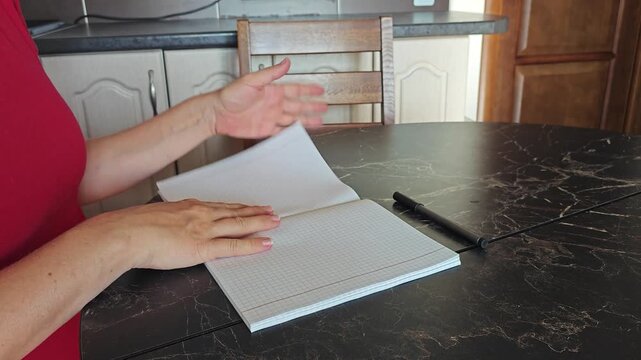 A pregnant girl at a table in the kitchen room leafs through a green notebook in a cage