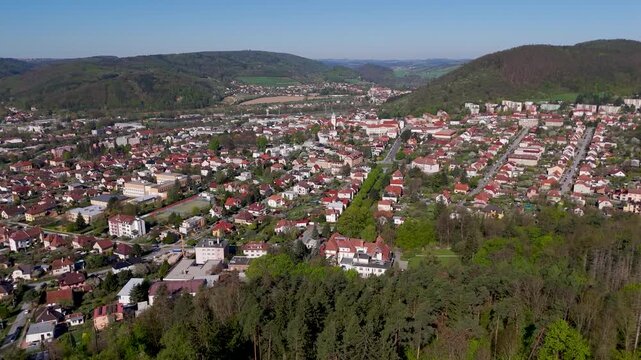 Expansive aerial extra wide shot of Tisnov town and surrounding Boskovice Furrow hills in Brno County, South Moravia, Czechia, showing residential areas and lush spring scenery.