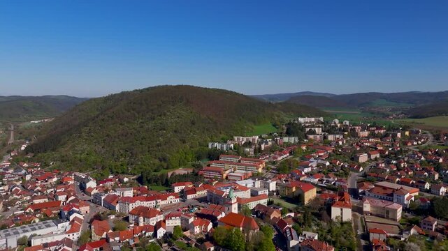 Wide aerial drone pan out revealing the residential town of Tisnov and the green Boskovice Furrow hills in South Moravia, Czech Republic, on a sunny spring day.