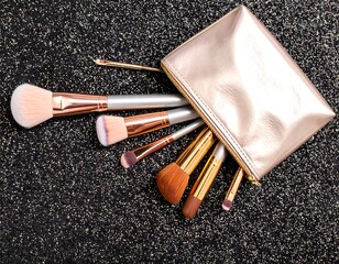 Makeup brushes in a gold pouch on a black glitter background