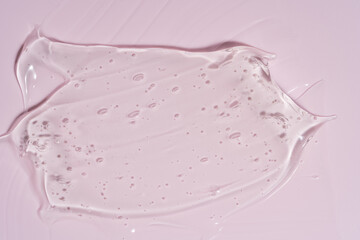 Close-up shot of pink liquid cosmetic gel or serum makeup swatches with a glossy, shiny texture on a smooth pink background
