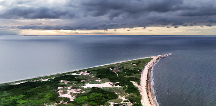 Aerial view of a narrow, grassy peninsula contrasts with the dark, brooding ocean under a stormy sky on Corn Neck Road, New Shoreham, Rhode Island, United States.