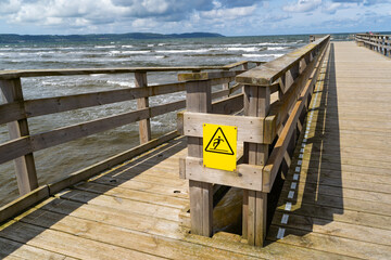 Enjoy a scenic wooden pier that features a caution sign, all while overlooking the sea