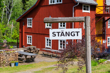 A sign reading CLOSED in front of a picturesque red wooden building in a serene outdoor setting, Sweden