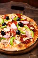 Pizza with chorizo ​​sausage, mozzarella cheese, green pepper and black olives. Rustic wooden background. Soft focus.	