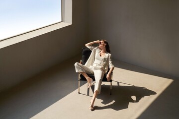 Woman in light summer outfit relaxing in modern interior with natural light.