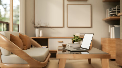 Blank screen laptop and coffee on glass top table and wooden sofa aside shelf in modern living room.
