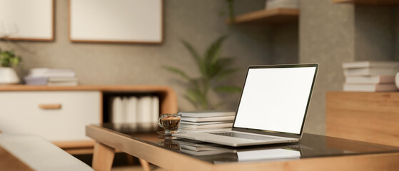 White screen laptop and coffee on glass top wooden table a aside bookshelf in a modern living room.