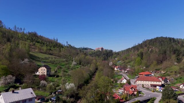 Majestic Pernstein Castle aerial view, dominating the traditional homes of Nedvedice village nestled within the lush green hills of South Moravia, Czech Republic.