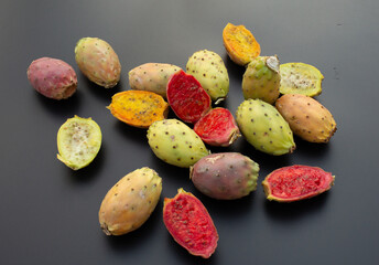 A top-down shot of ripe prickly pears in multiple shades scattered on black background.
