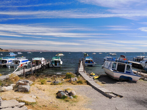 Photo of small harbour in Copacabana at Lake Titicaca in Bolivia. Golden sand, green water, blue sky with white flat clouds, many tourist boats in the water.