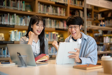 Glasses asian man student and woman friend looking at tablet and making a fist at table in library.