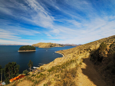 Picturesque landscape of Isla del Sol on Titicaca Lake in Bolivia. Yellow dry vegetation, deep blue lake, blue sky with gentle white clouds.