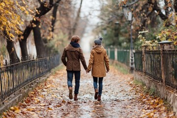 Fototapeta premium Young couple holding hands while walking through autumn park
