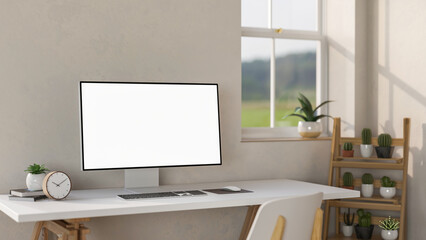 Blank screen computer aside clock and potted plant on white table aside wooden display shelf.