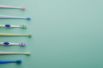 Group of assorted color toothbrushes lined up on a pastel green background, creative composition.