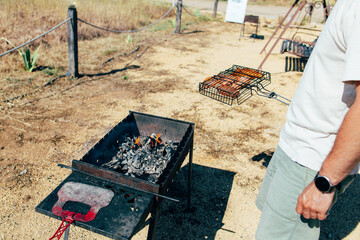 Meat being cooked on a barbecue grill over an open fire in a field. Outdoor cooking, camping, family vacation