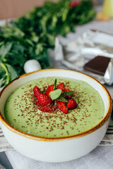 Ready green smoothie in a bowl with strawberries and dark chocolate. Suitable for advertising healthy eating, fitness brands, cafes, blogs and menus	