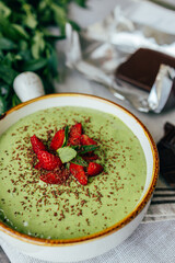 Ready green smoothie in a bowl with strawberries and dark chocolate. Suitable for advertising healthy eating, fitness brands, cafes, blogs and menus	