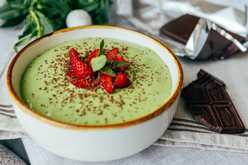 Ready green smoothie in a bowl with strawberries and dark chocolate. Suitable for advertising healthy eating, fitness brands, cafes, blogs and menus	