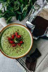 Ready green smoothie in a bowl with strawberries and dark chocolate. Suitable for advertising healthy eating, fitness brands, cafes, blogs and menus	