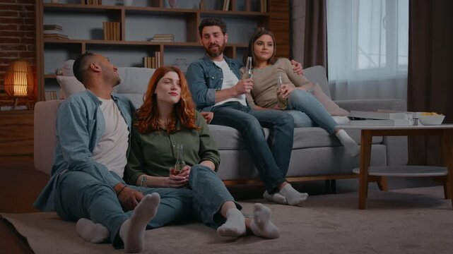 Multiracial four friends spending time watching tv hanging out at home party watch television pleasant weekend talking men funny discuss laughing smiling women enjoying cinema movie program relaxing