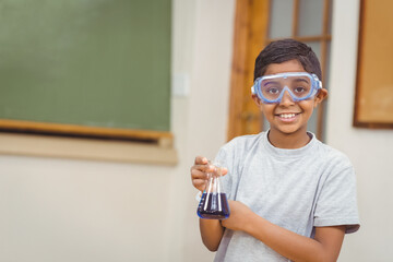 Conical flask holding dark blue liquid is resting on classroom desk, near green chalkboard
