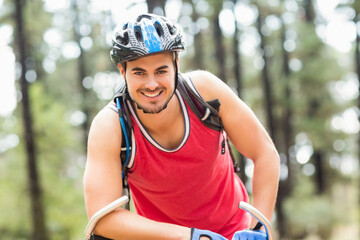 Fototapeta premium Smiling male cyclist wearing bike helmet leaning on forest trail handlebars, with hydration pack