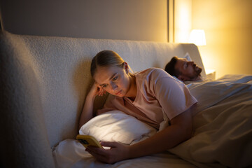 Sleepless tired woman awake late, scrolling smartphone browsing social media, web feed in bed. Female focused on digital feed, losing track of time to online activity, digital addiction, insomnia