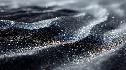 Shimmering black sand with silver sparkles creates mesmerizing wave-like patterns in dramatic macro photography, highlighting natural texture and light reflection.