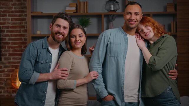 Four happy multiracial friends posing together at home party smiling looking at camera diversity two couples indoors positive multiethnic men women portrait in living room teammates buddies cuddling