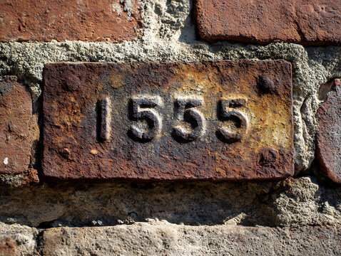 Close up of a weathered brick with the embossed year 1555 in a historic wall - Powered by Adobe